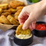 Hand dipping a fried zucchini bite into creamy sauce.