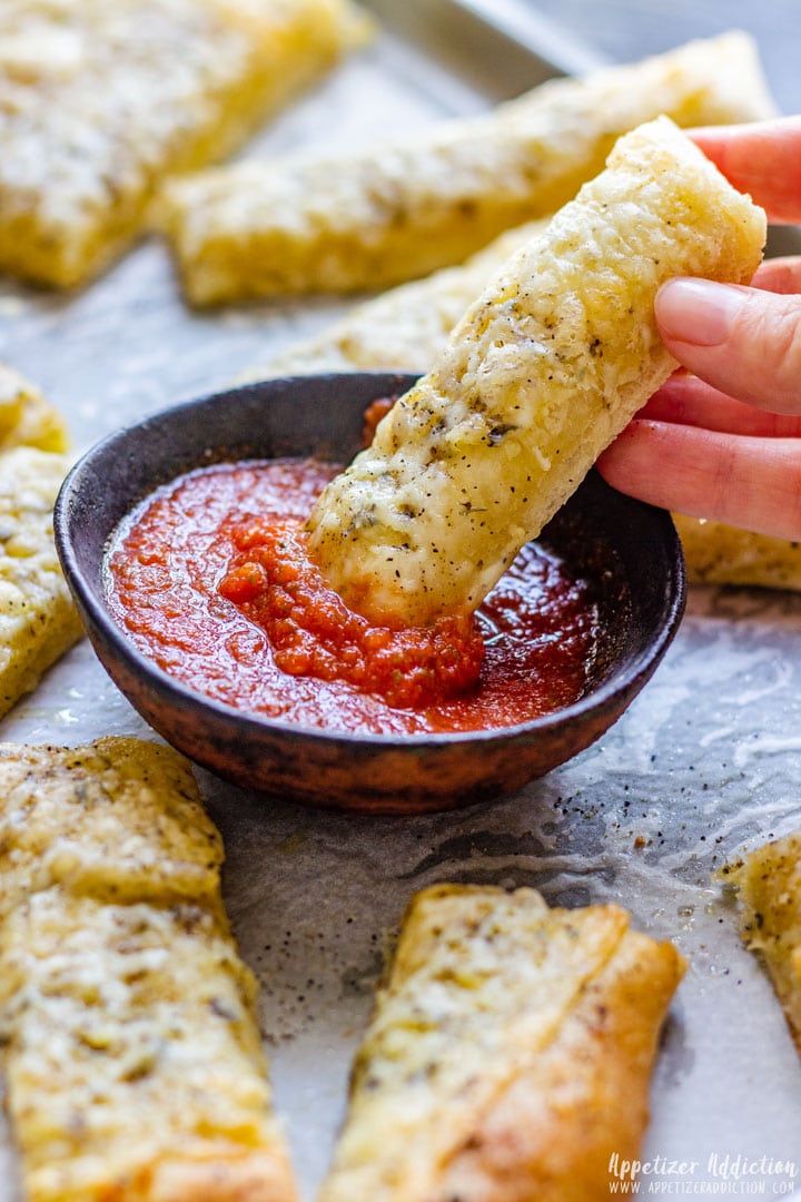 Homemade pizza dough breadsticks with red sauce.
