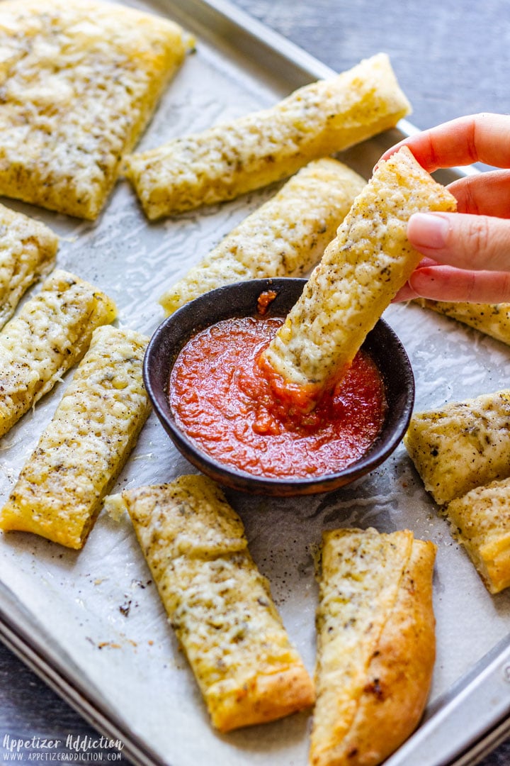 Dipping pizza dough breadstick to pizza sauce.