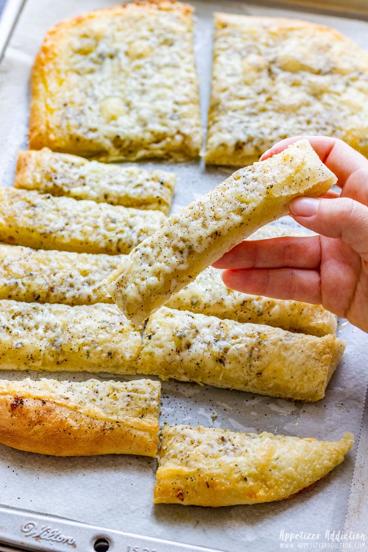 Holding a sliced pizza dough breadstick covered with cheese.