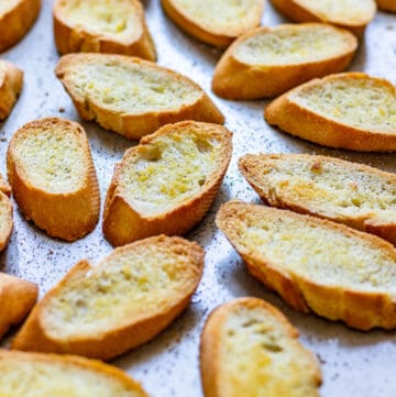 Golden oven crostini made from sliced baguette on a baking sheet.