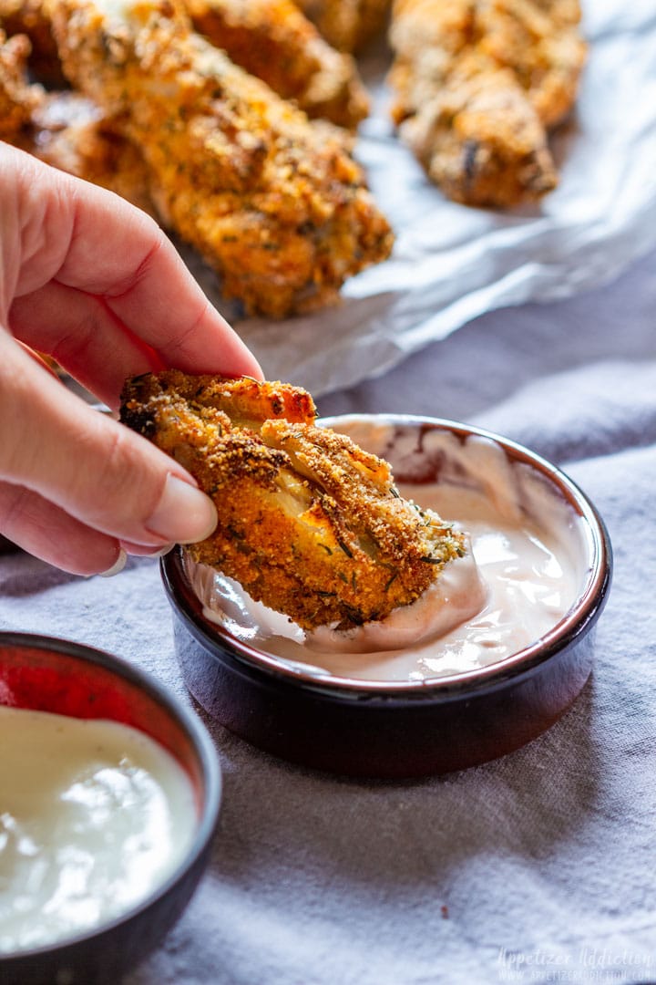 Oven baked chicken wing being dipped into a spicy garlic sauce