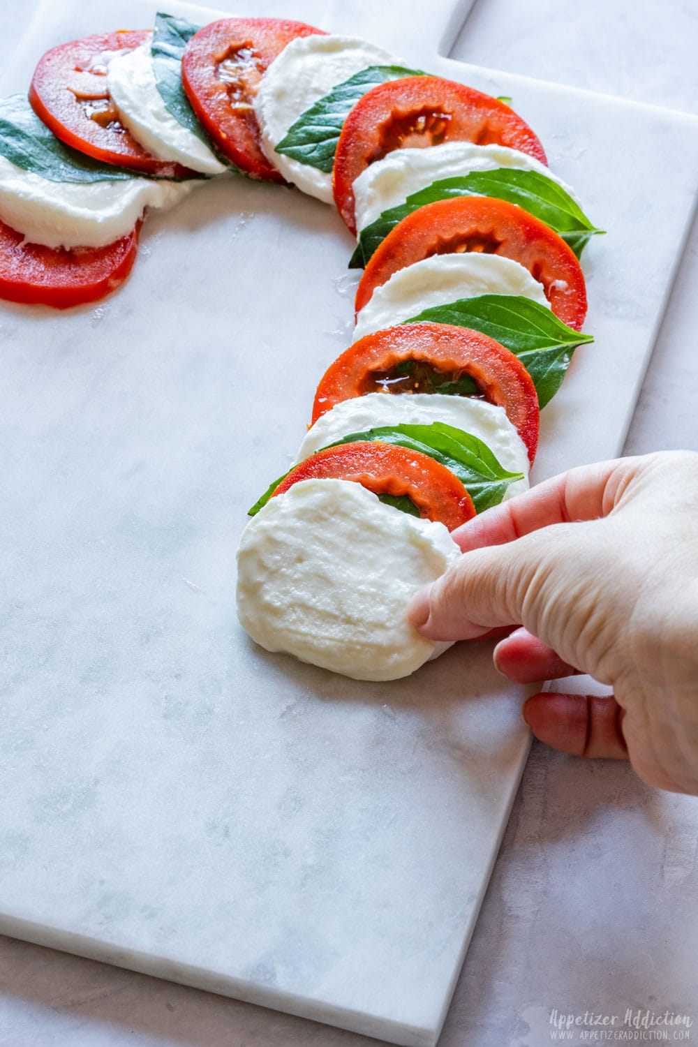 Placing sliced mozzarella to Caprese board shaped as candy cane.