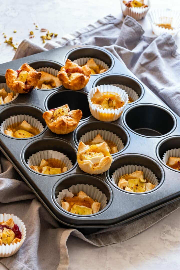 Freshly baked puff pasty brie bites on a muffin tray.