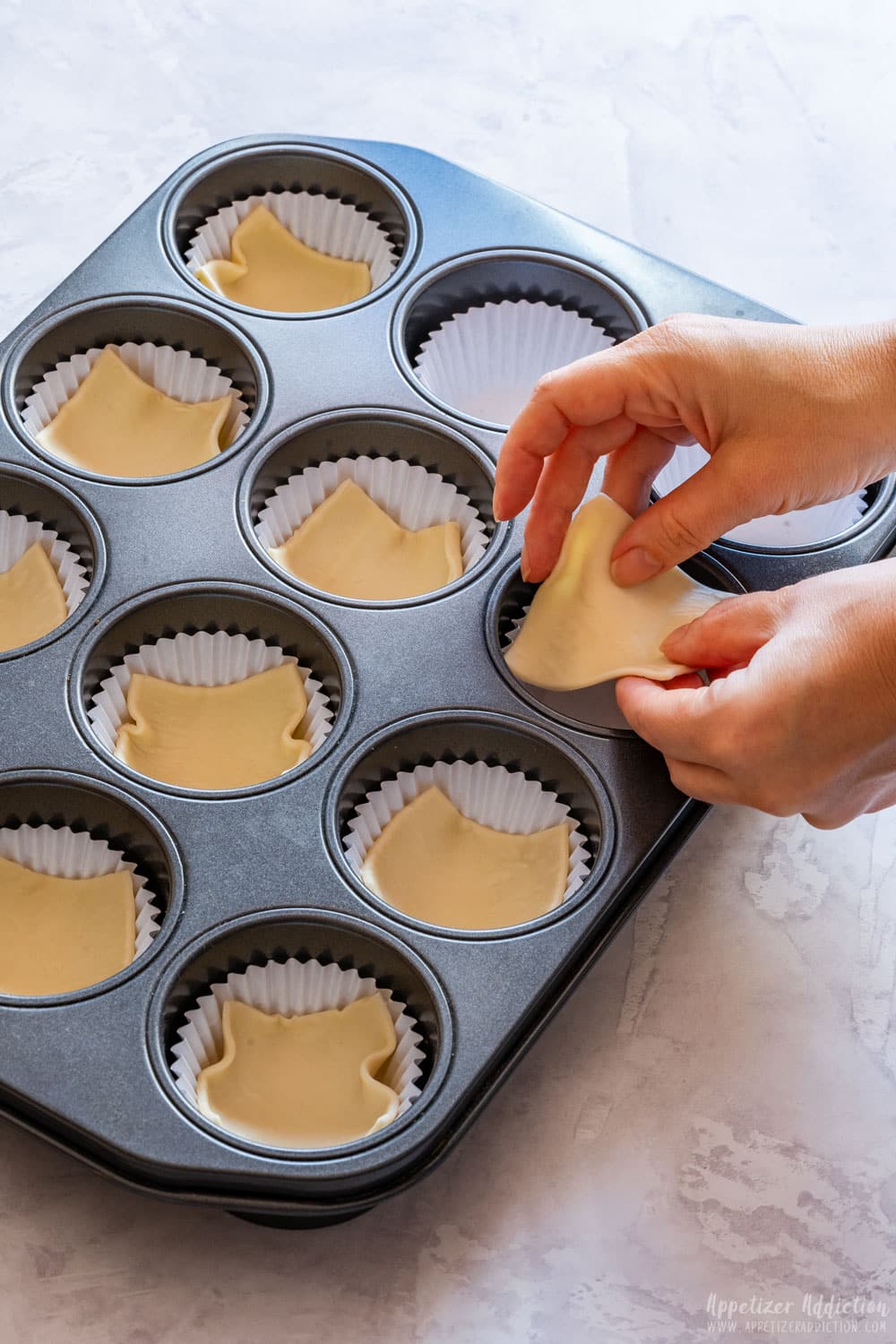 Filling muffin tray with puff pastry squares.