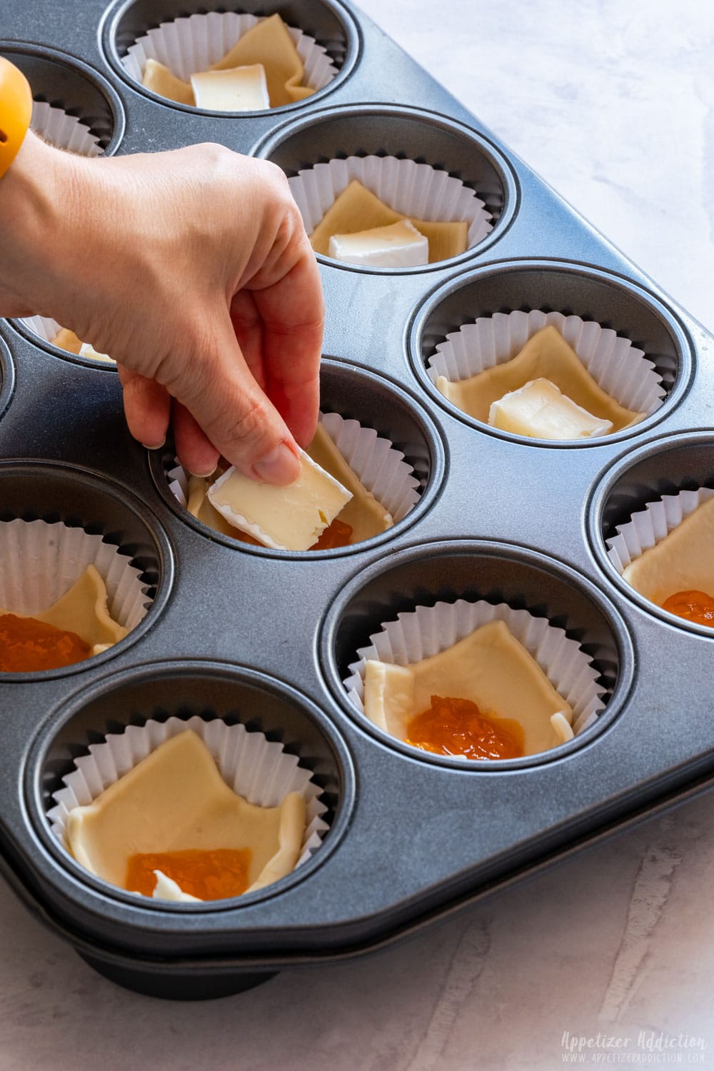 Adding brie cheese to the puff pastry appetizers.