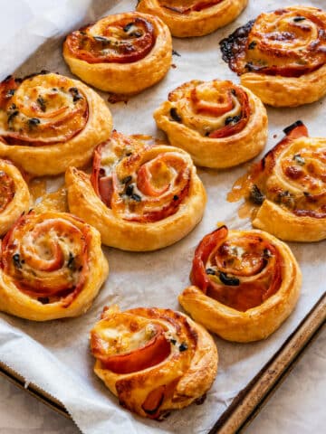 Freshly baked puff pastry ham and cheese pinwheels on the baking tray.