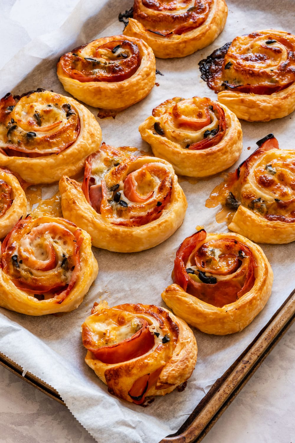 Freshly baked puff pastry ham and cheese pinwheels on the baking tray.