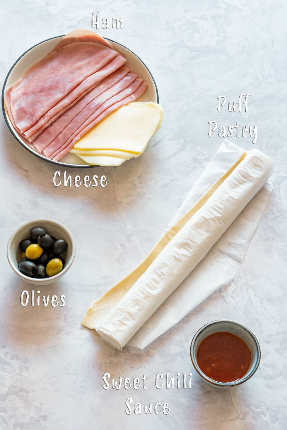 Ingredients for ham and cheese pinwheels - puff pastry, ham, cheese, olives and chili sauce.