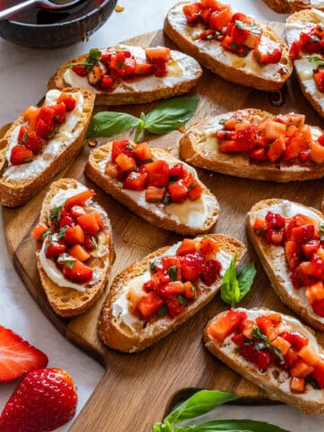 Strawberry bruschetta with fresh basil leaves on a wooden tray.