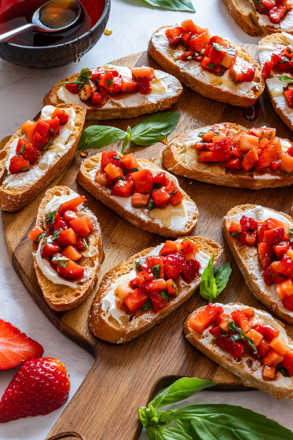 Strawberry bruschetta with fresh basil leaves on a wooden tray.
