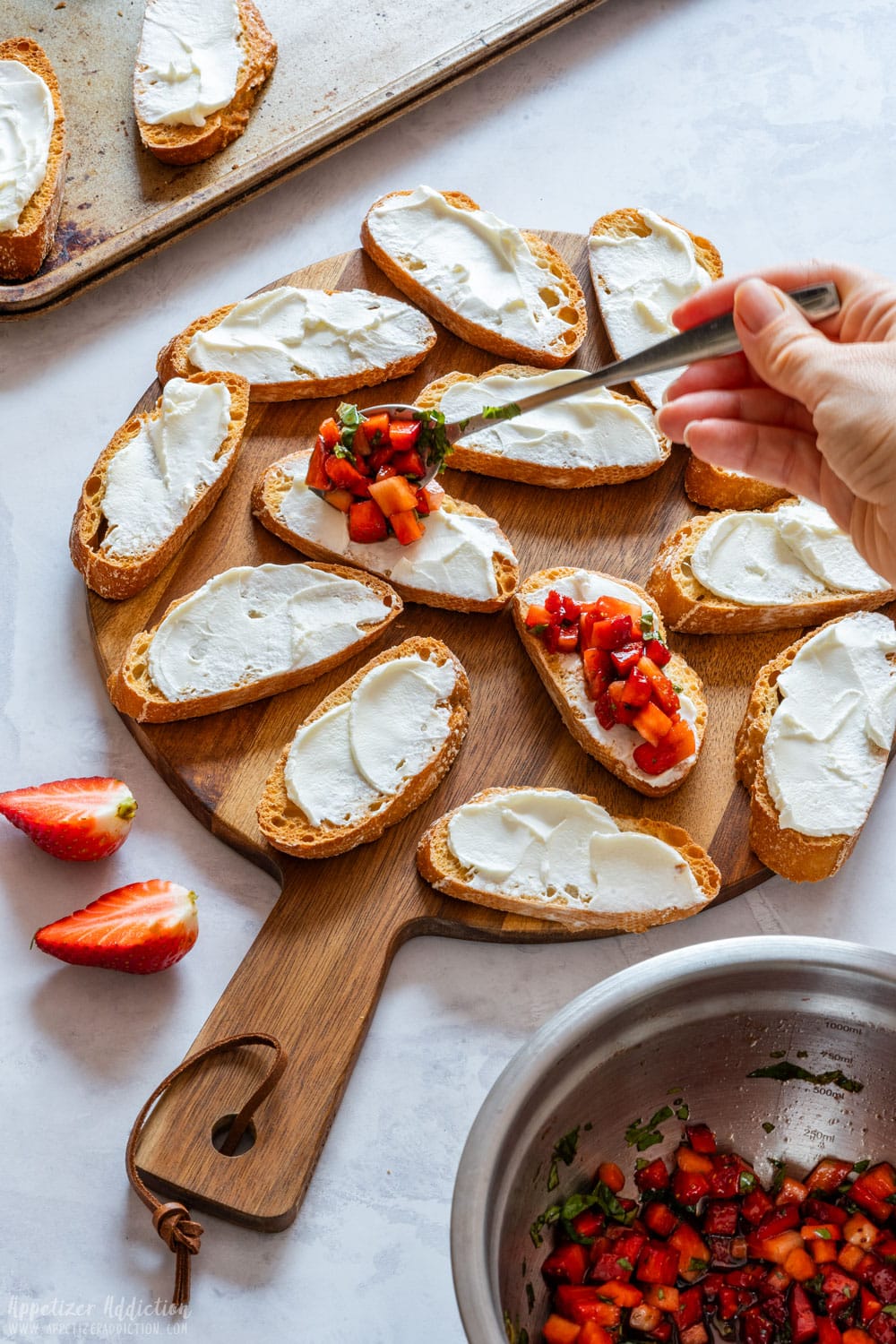 Adding topping to cream cheese covered toasted French baguette slice.