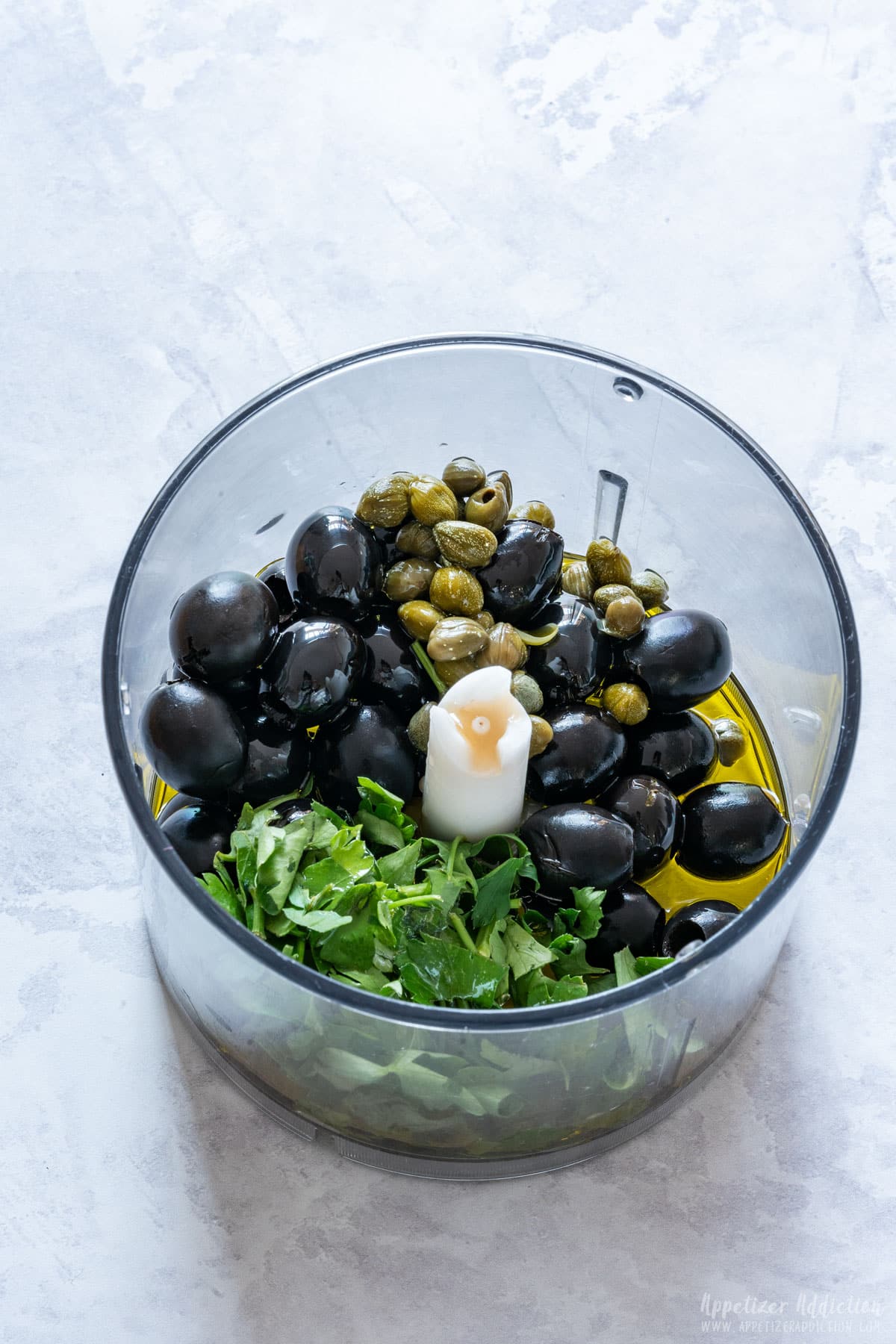 Black olives, capers, fresh parsley and olive oil in the food processor bowl.