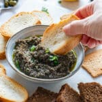 Scooping black olive tapenade with crostini.