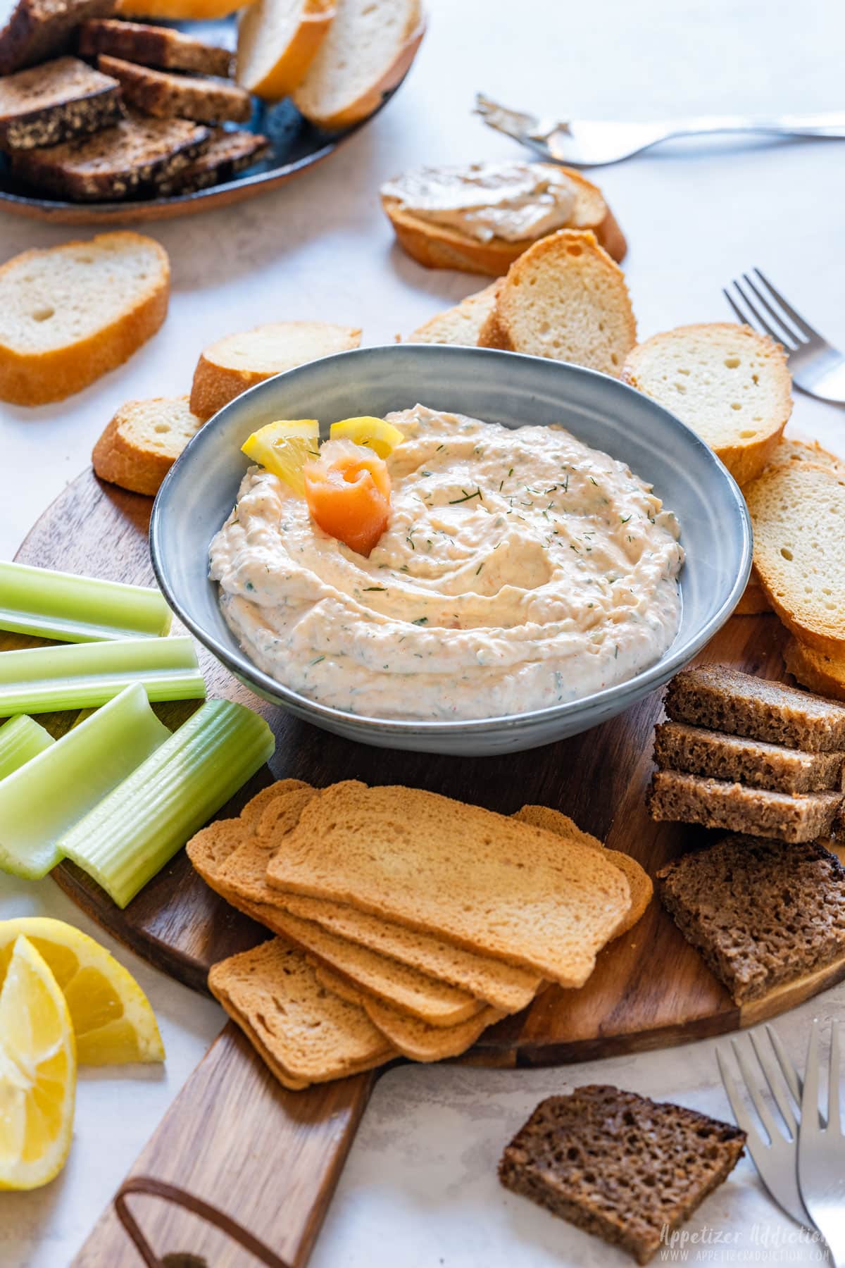 Smoked salmon dip with breads and celery on a wooden tray.