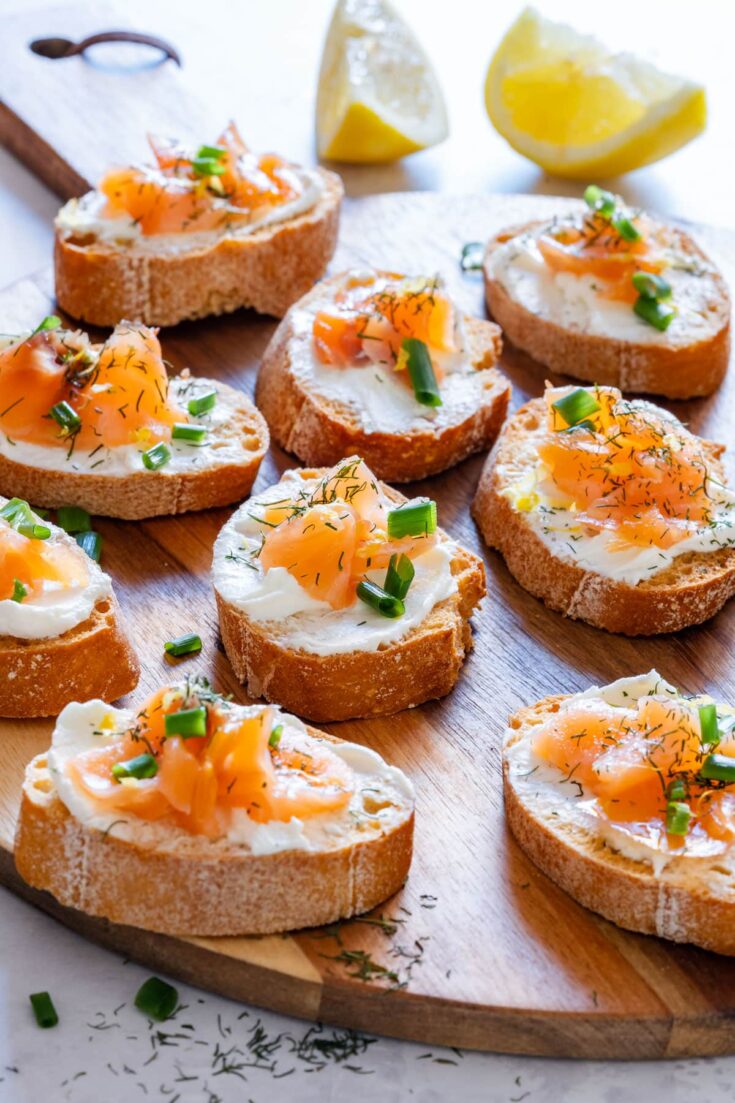 Smoked salmon crostini with cream cheese and dill on wooden serving tray.