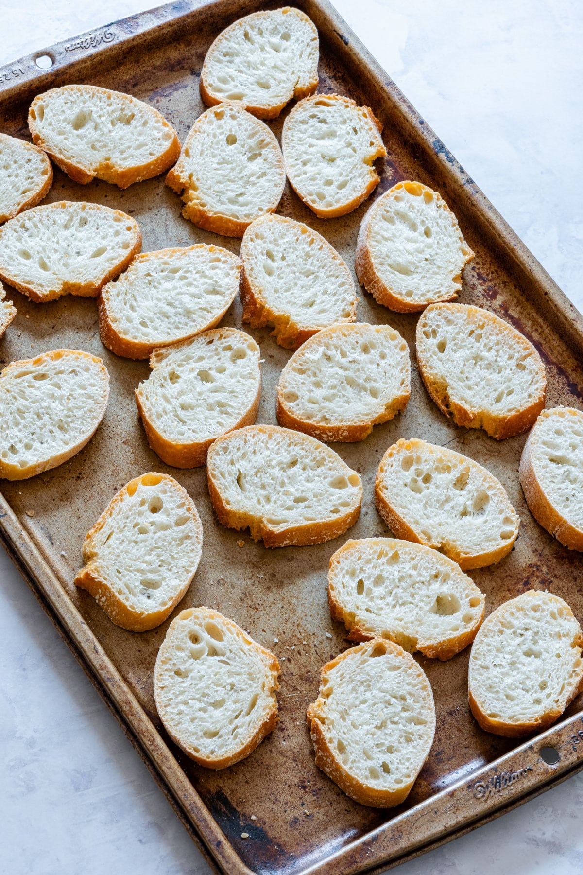 French baguette slices on the baking tray before baking.