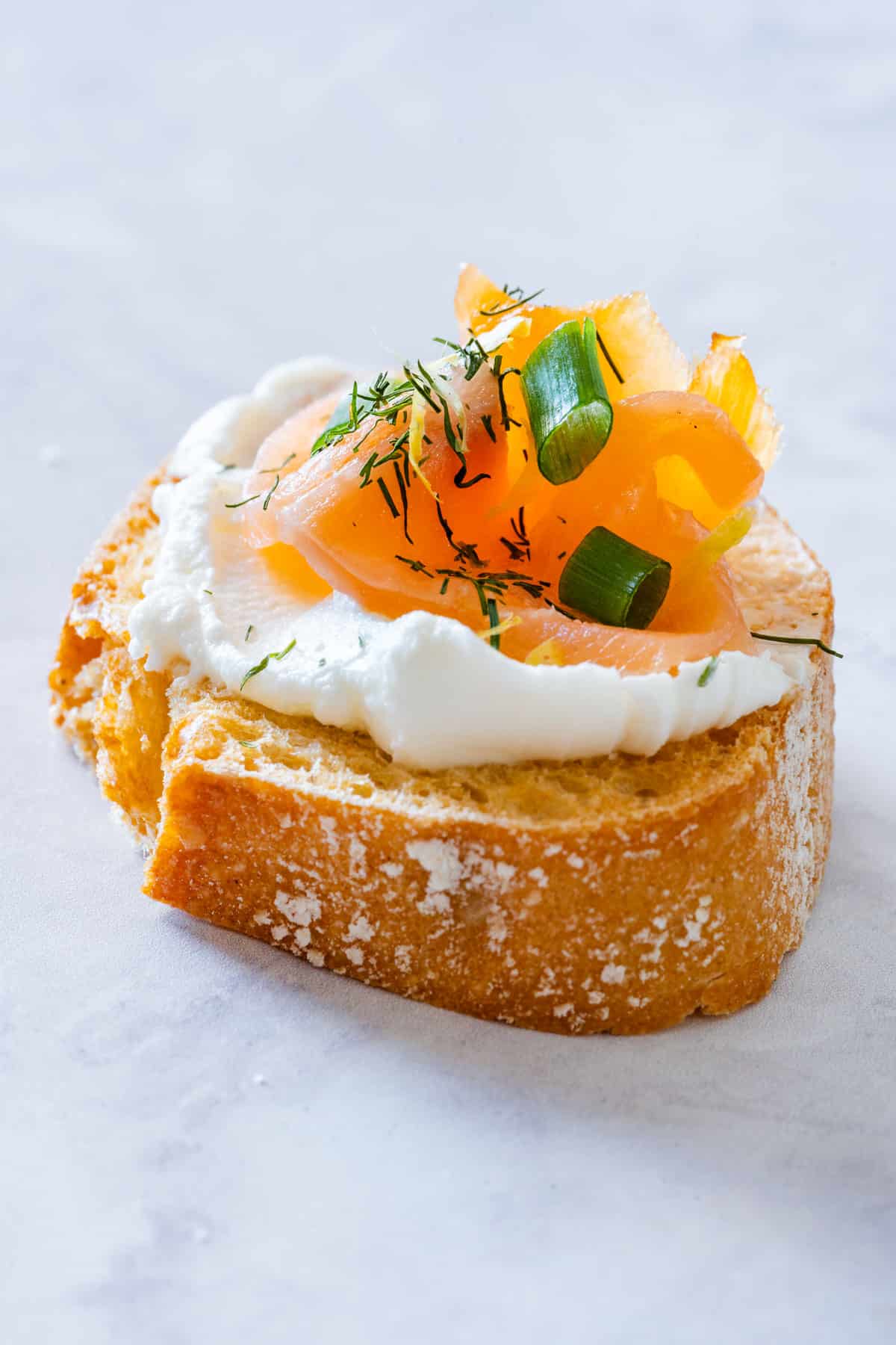 Close-up of crispy crostini topped with cream cheese, smoked salmon and dill.