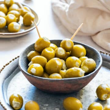 Bowl of green olives stuffed with creamy blue cheese, served on a rustic metal tray with toothpicks.