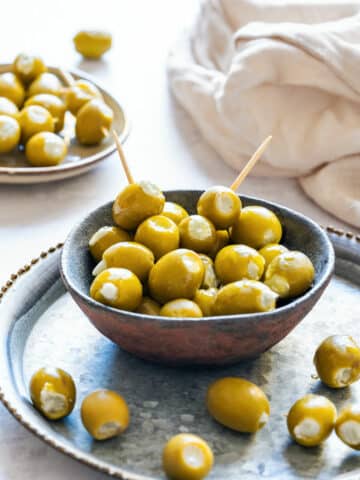 Bowl of green olives stuffed with creamy blue cheese, served on a rustic metal tray with toothpicks.