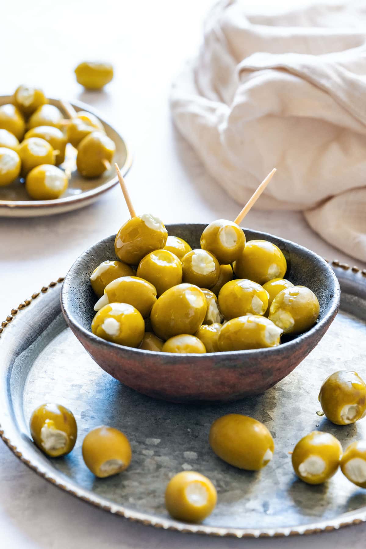 Bowl of green olives stuffed with creamy blue cheese, served on a rustic metal tray with toothpicks.