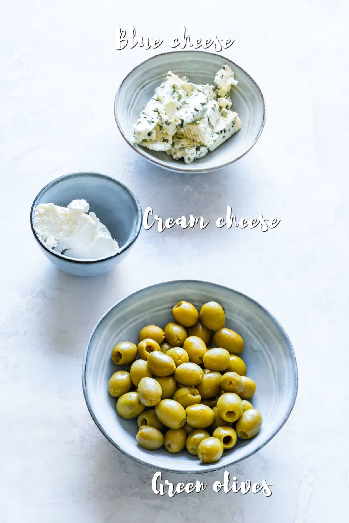 Ingredients for blue cheese stuffed olives: green olives, blue cheese and cream cheese in ceramic bowls.