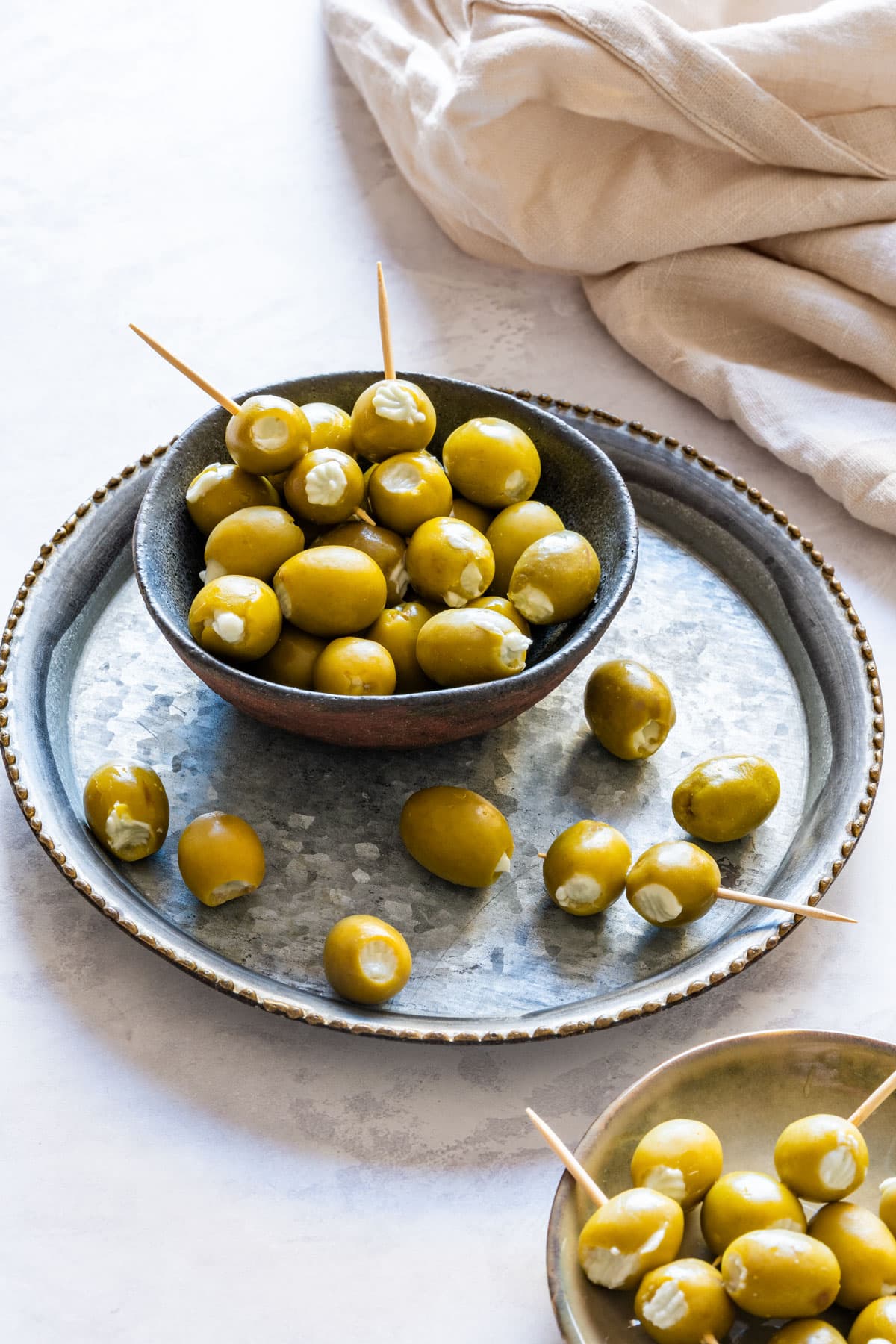 Two small bowls filled with green olives stuffed with creamy blue cheese, served with toothpicks.