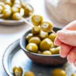 Hand holding a toothpick with two blue cheese stuffed olives.