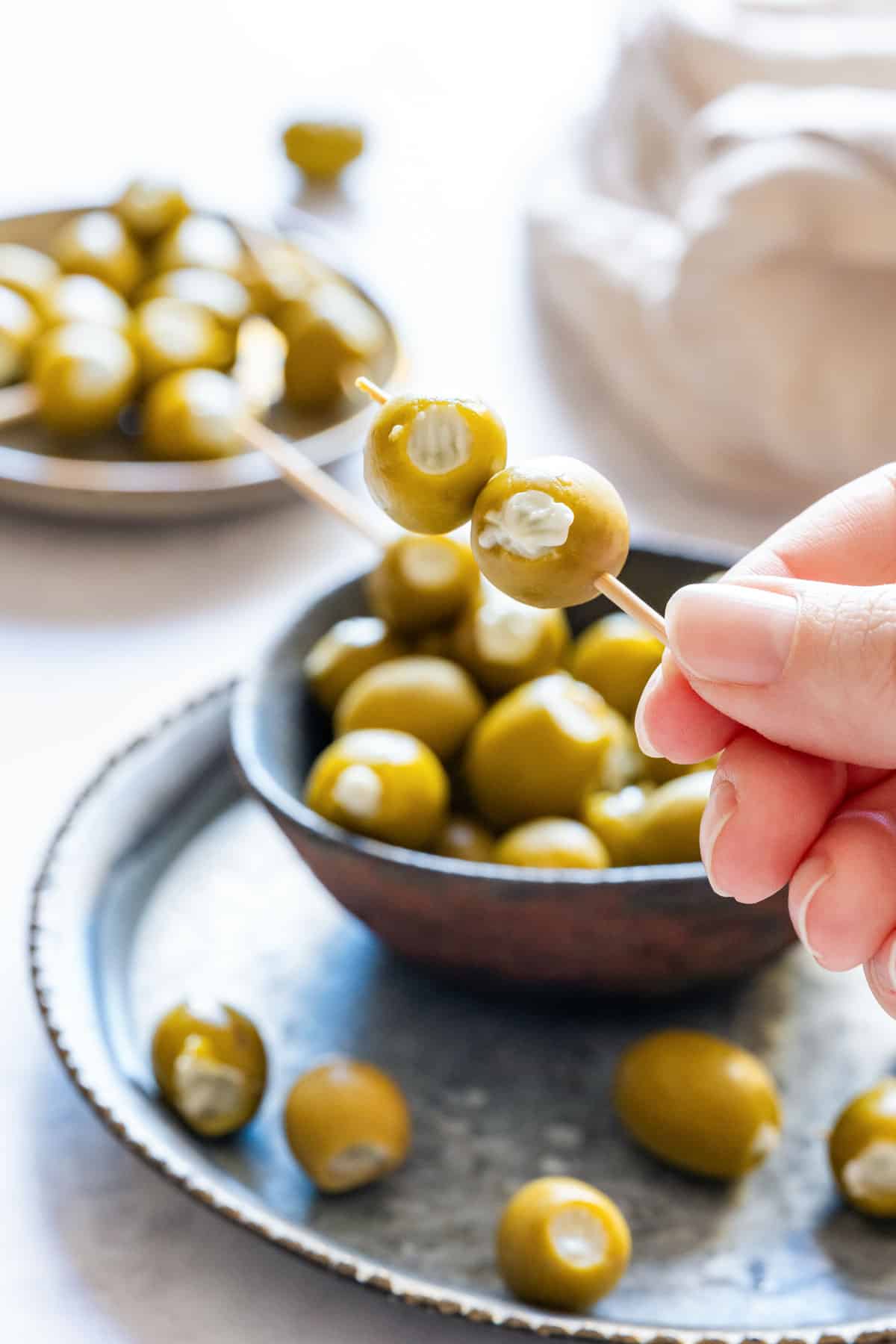 Hand holding a toothpick with two blue cheese stuffed olives.