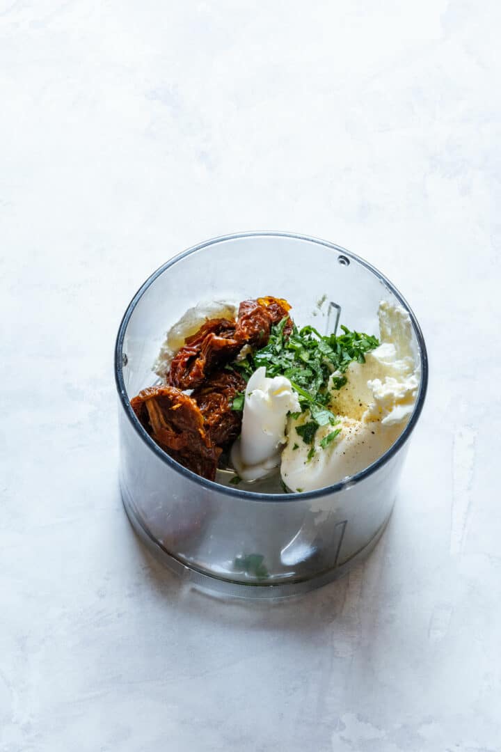 Ingredients placed in a food processor: sun-dried tomatoes, cream cheese, parsley and seasoning.