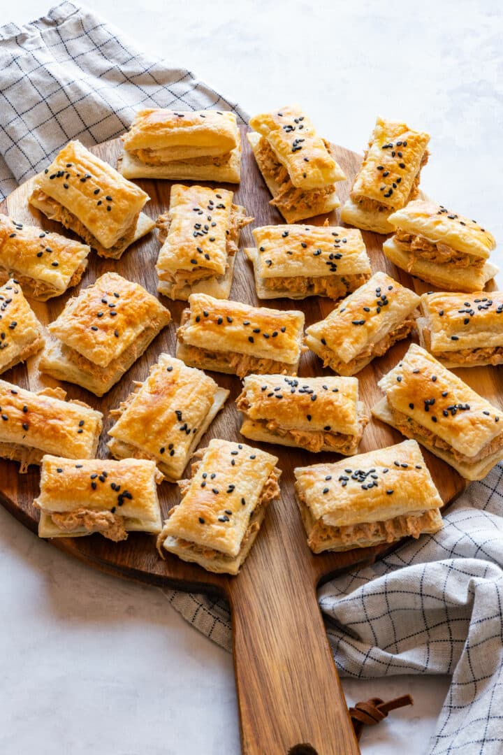 Baked and filled sun-dried tomato chicken puffs on a serving board with a tea towel.