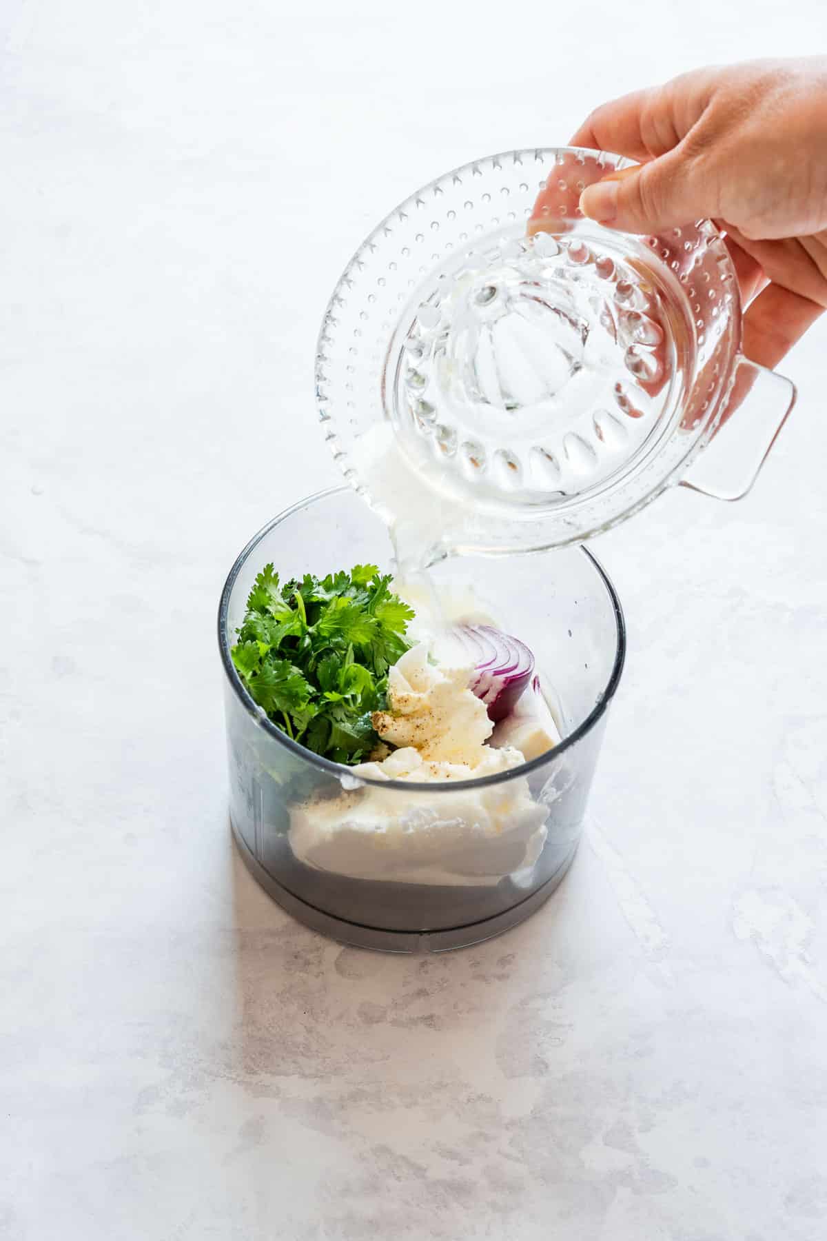 Pouring fresh lemon juice into a food processor with cilantro, red onion, cream cheese and yogurt.
