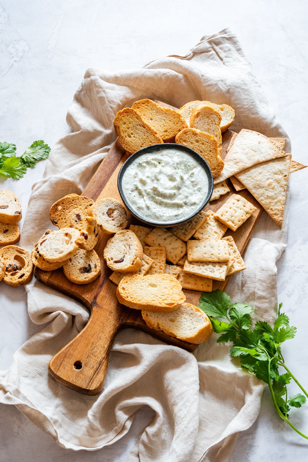 Overhead view of a small bowl of cilantro dip on a wooden board with toast slices and crackers.