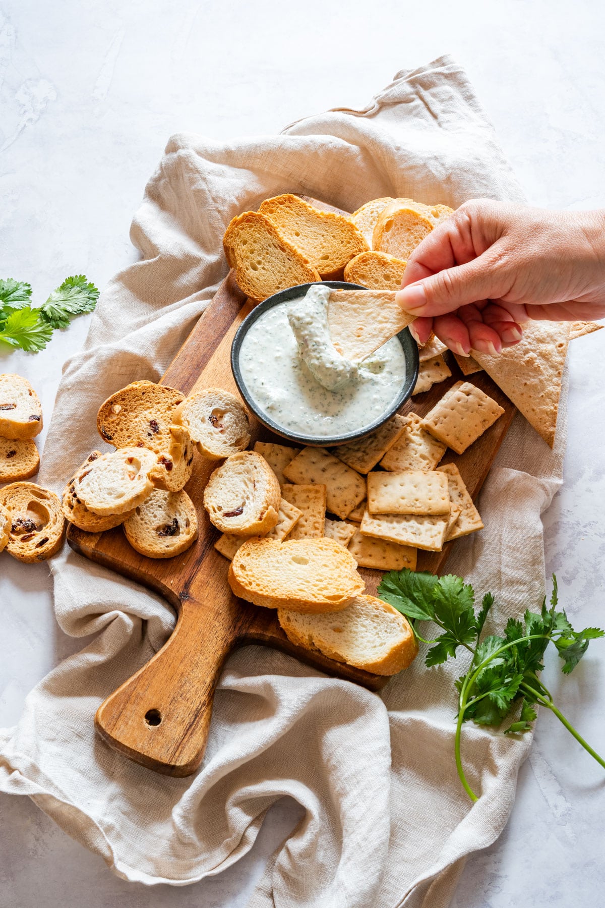 Close-up of a tortilla chip scooping creamy cilantro dip from a black bowl on a wooden serving board.