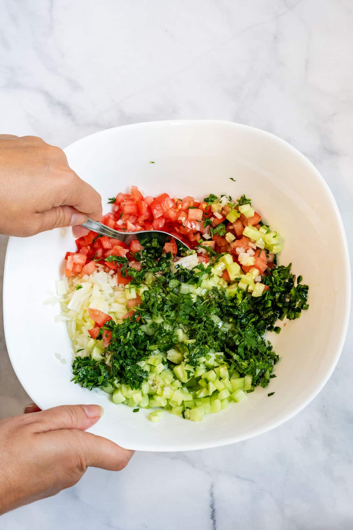 Julia mixing with spoon cucumber salsa ingredients together in a white bowl.