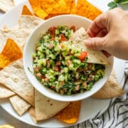 Hand dipping a tortilla chip into colorful cucumber salsa.