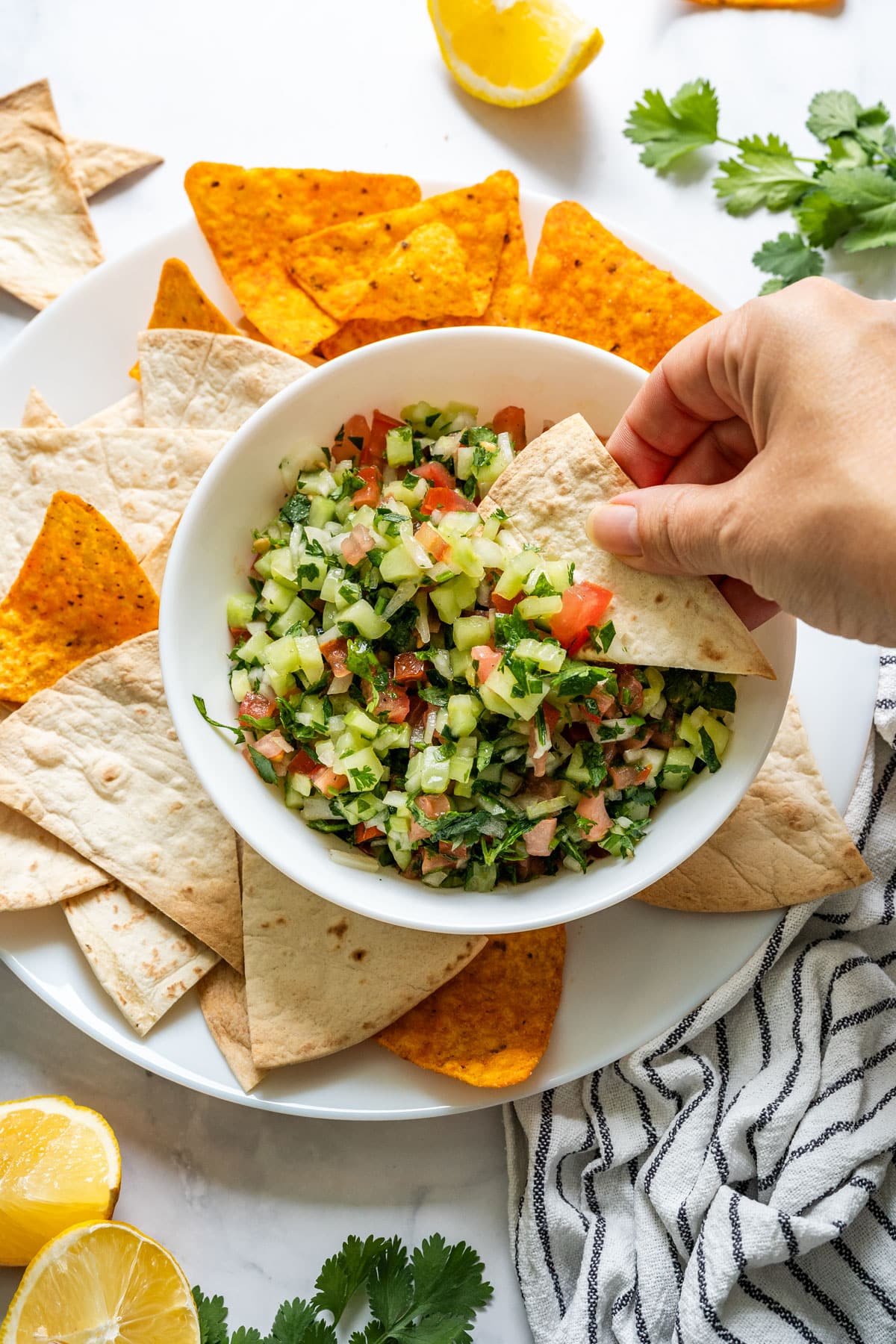 Hand dipping a tortilla chip into colorful cucumber salsa.