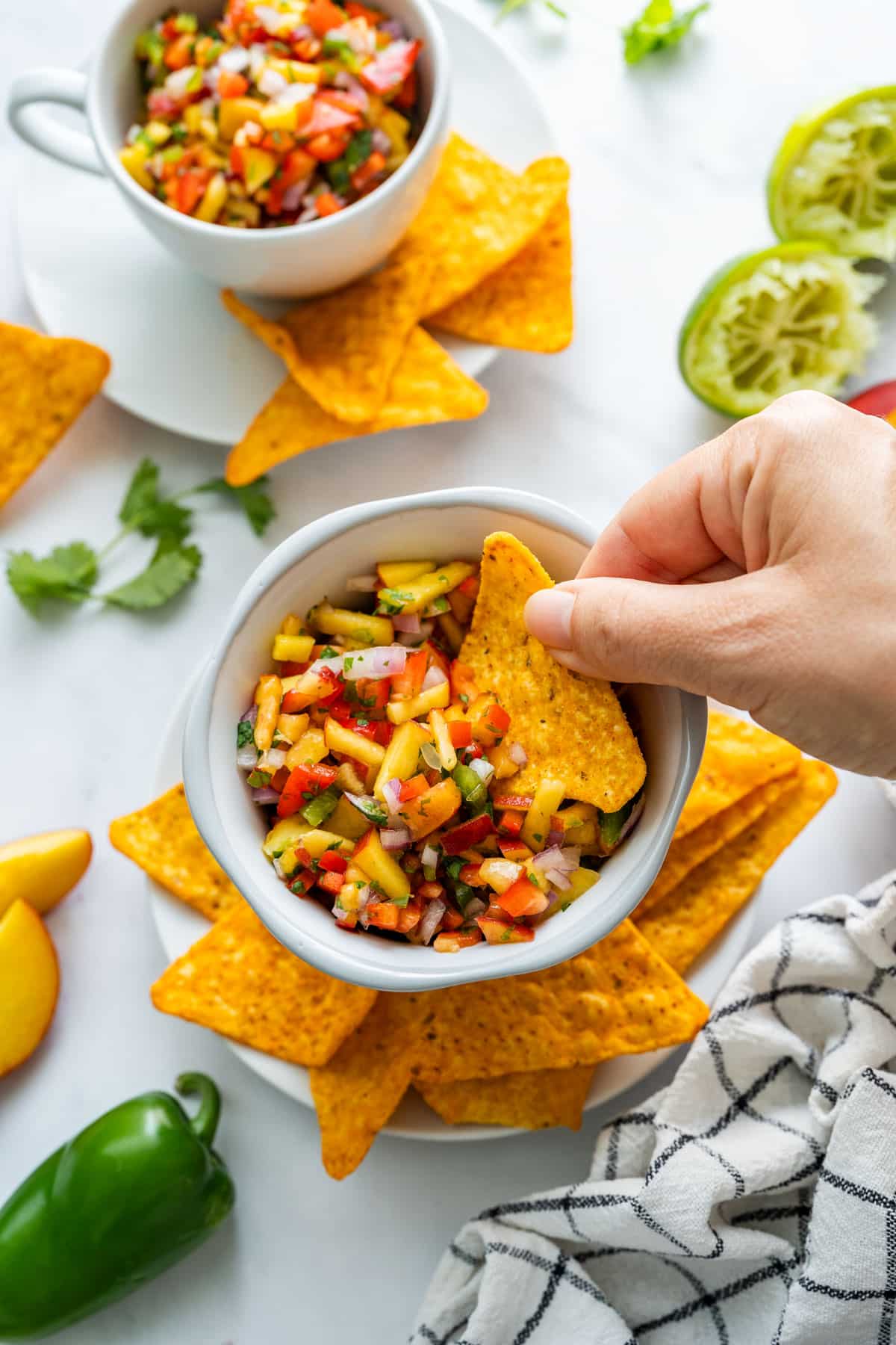 A hand dipping a tortilla chip into a bowl of peach salsa.
