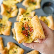 Hand holding a mini quiche with visible vegetable filling.