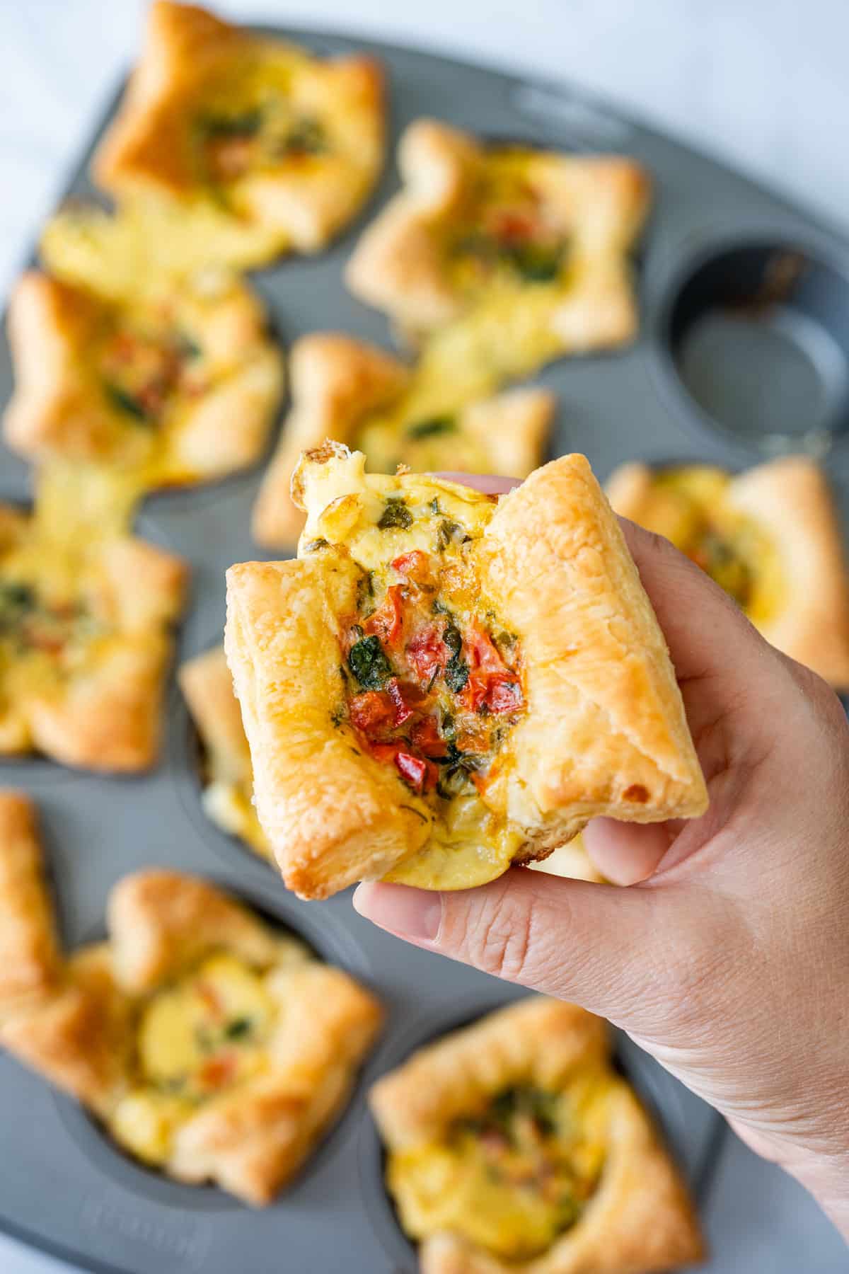 Hand holding a mini quiche with visible vegetable filling.