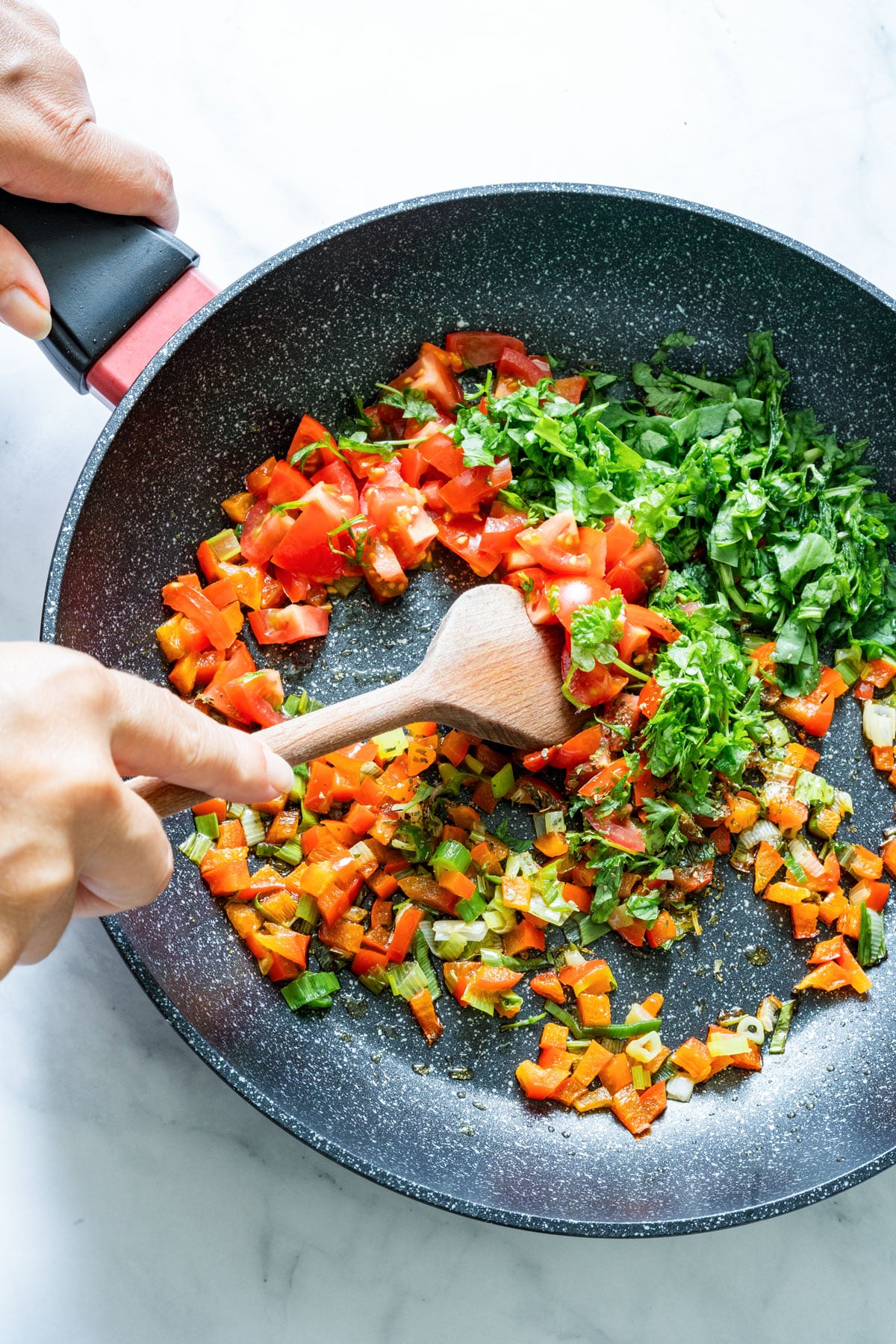 Chopped vegetables and herbs cooking in a frying pan.