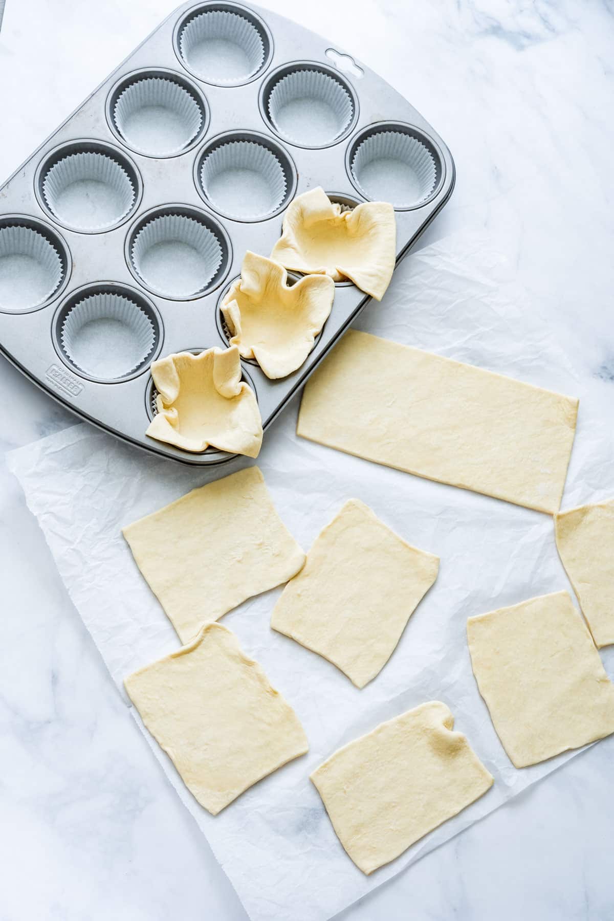Puff pastry sheets cut into squares beside a muffin tin.