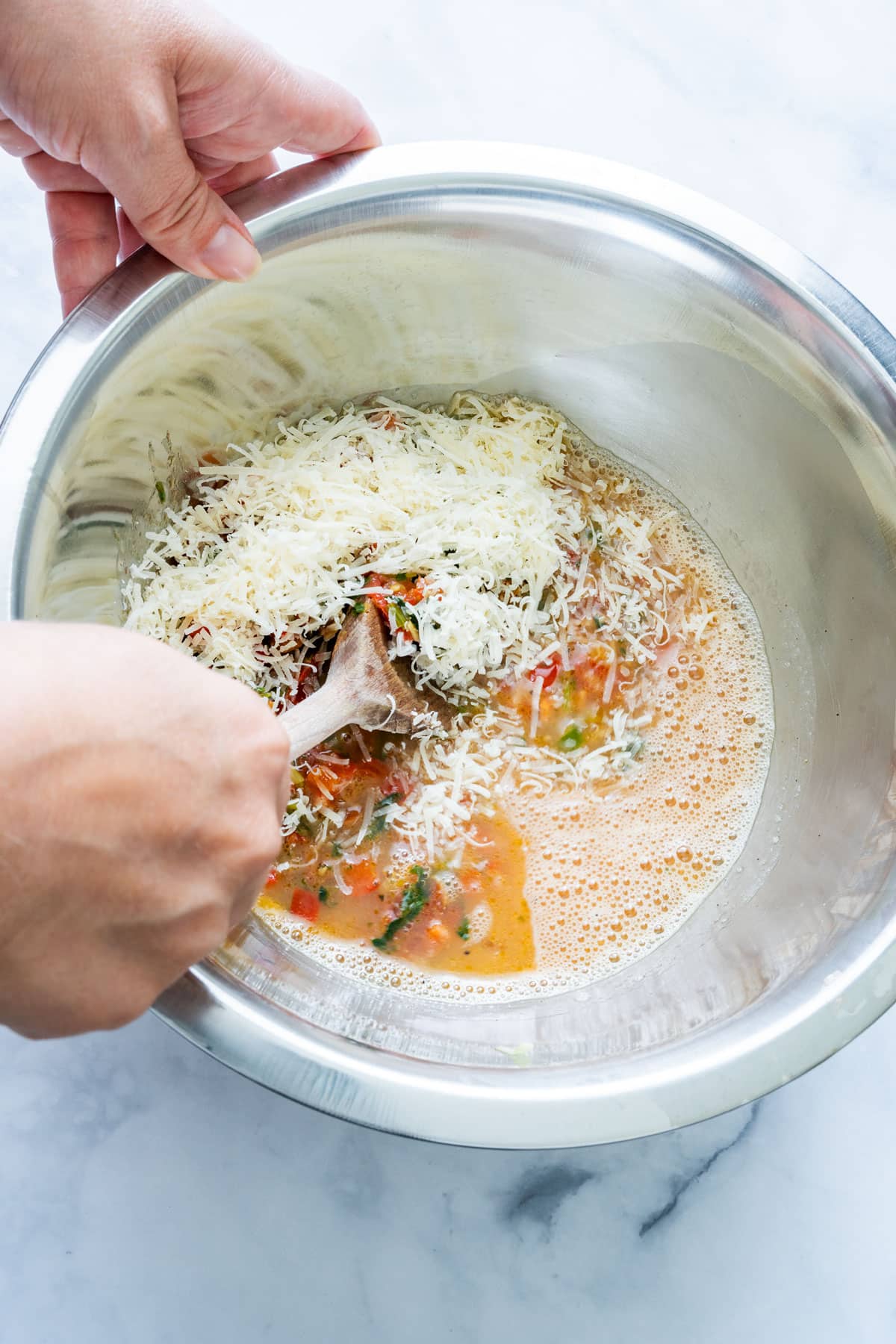 Mixing grated cheese into whisked eggs and vegetables.