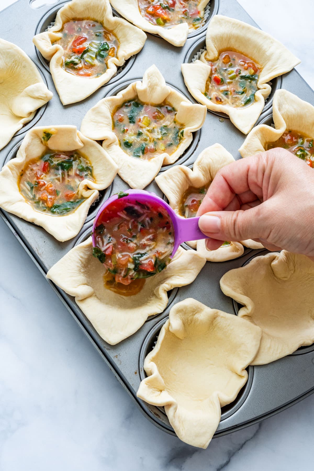 Spoonful of quiche filling being added to pastry cups.