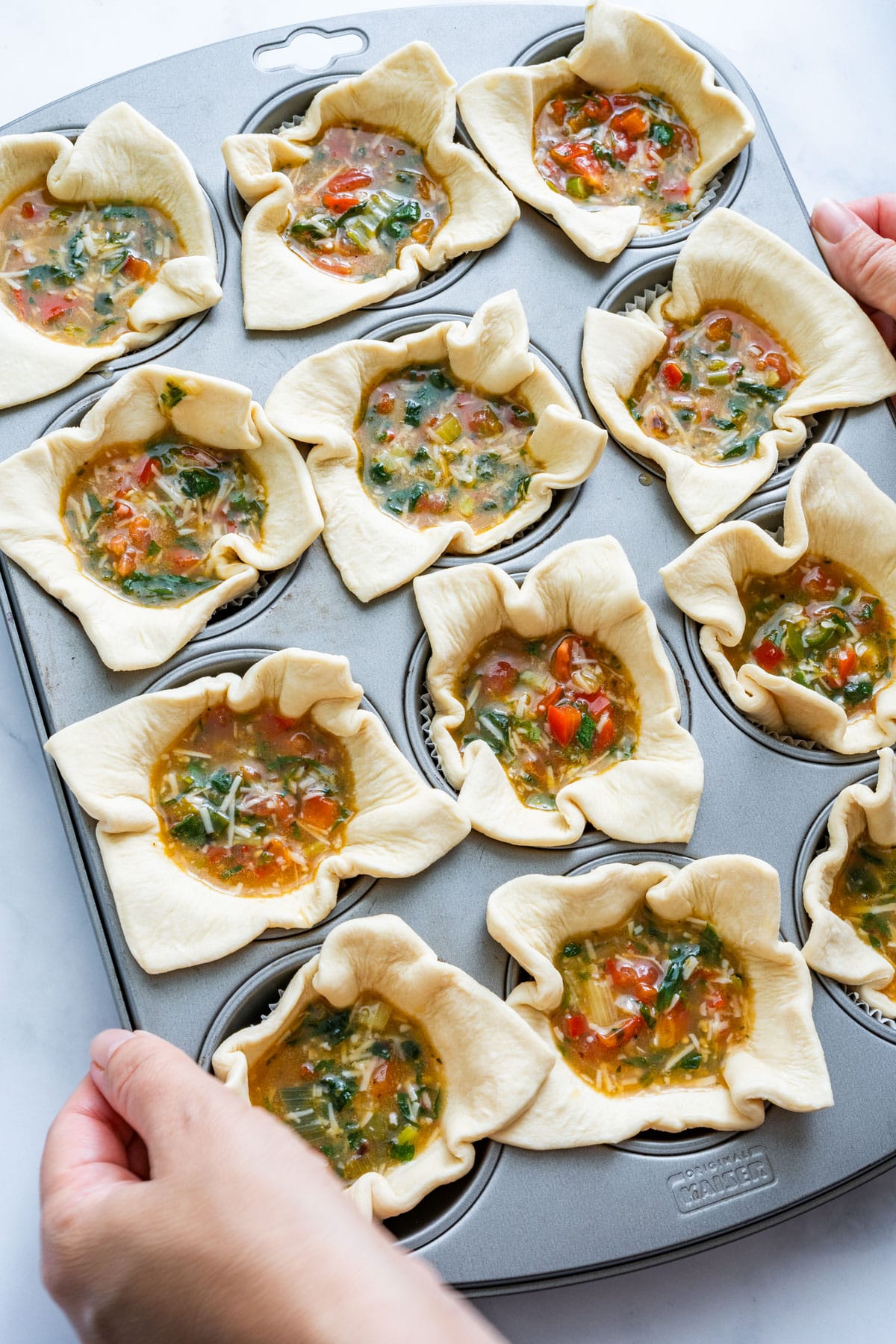 Muffin tin filled with puff pastry and vegetable egg mixture.