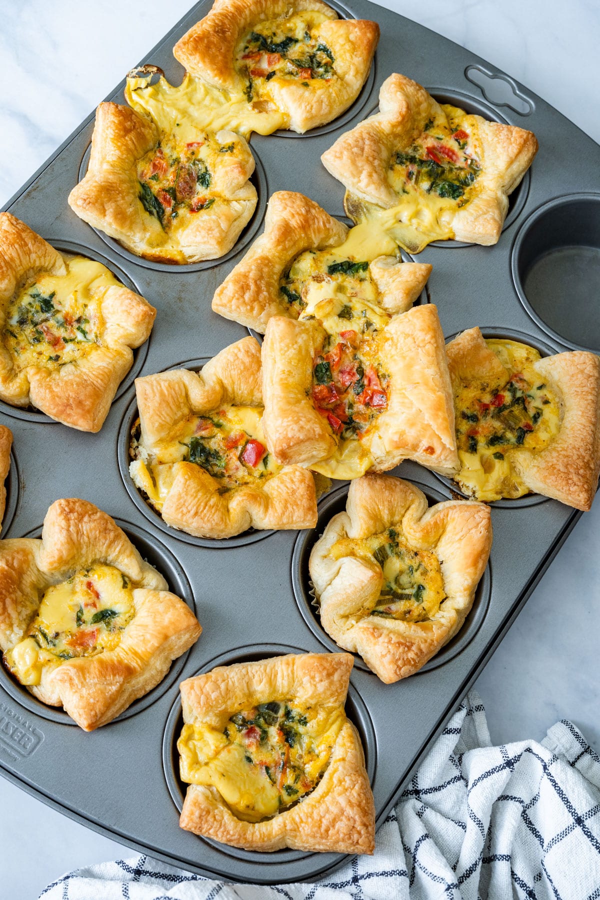 Freshly baked golden mini quiches cooling in the muffin tin.