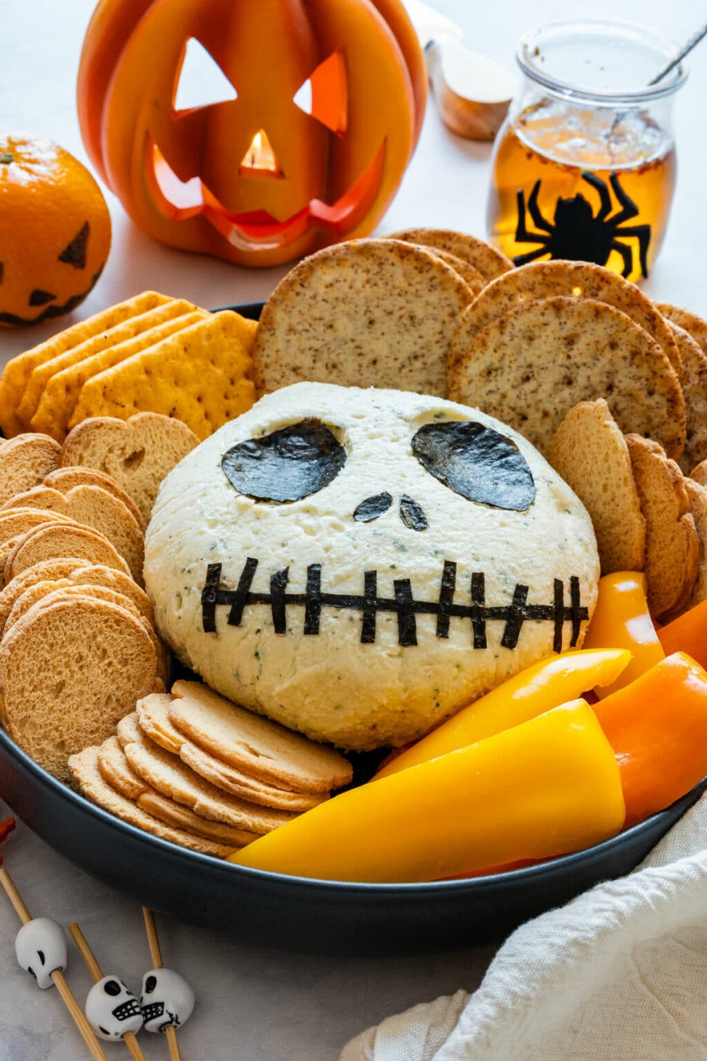Finished Jack Skellington cheese ball on a serving platter with crackers and sliced peppers.