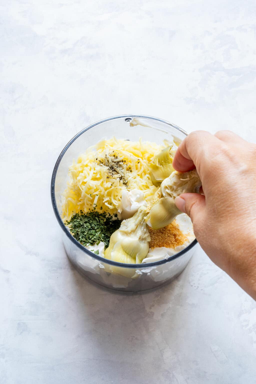 Adding artichoke hearts to a food processor with cream cheese, cheddar and seasonings.