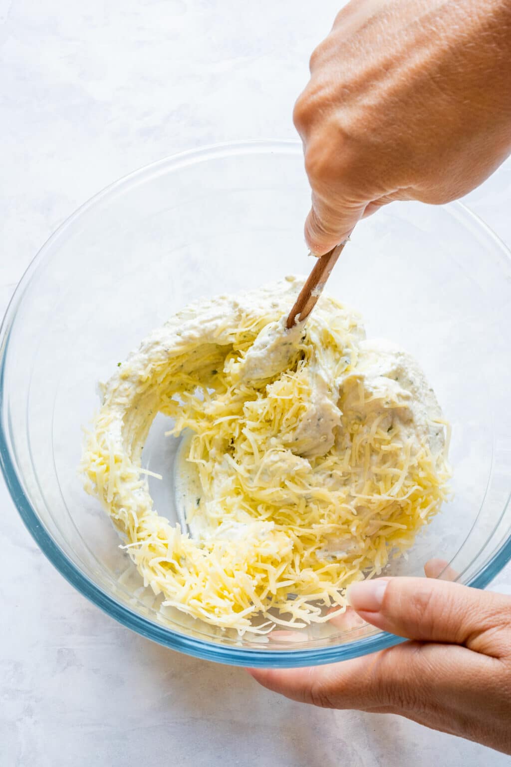 Folding shredded cheddar into the creamy artichoke mixture.
