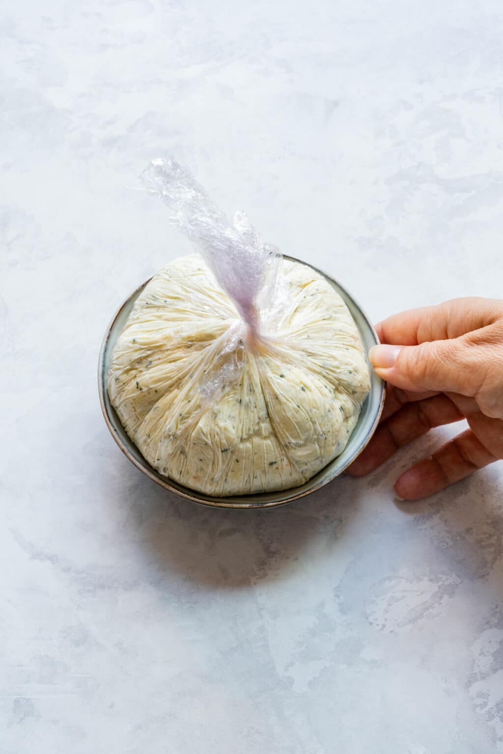 Cheese ball wrapped in plastic wrap and set in a bowl to chill.
